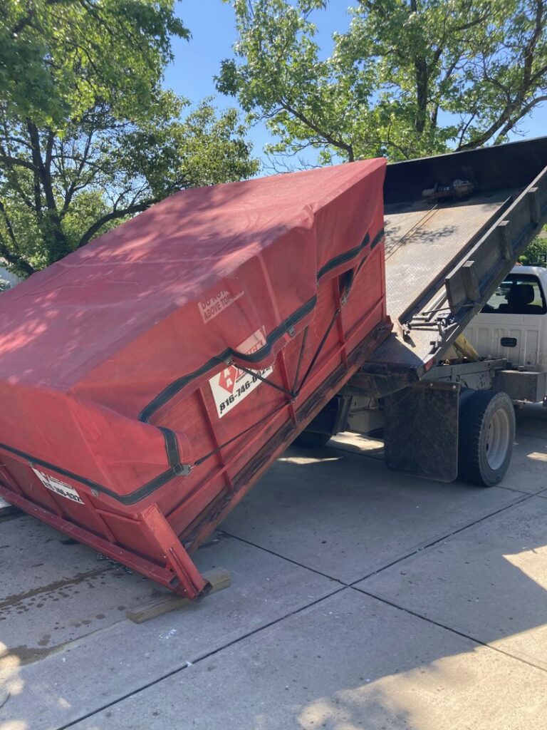 An AA Quick Disposal truck unloading a red dumpster for junk removal service in Kansas City, MO.