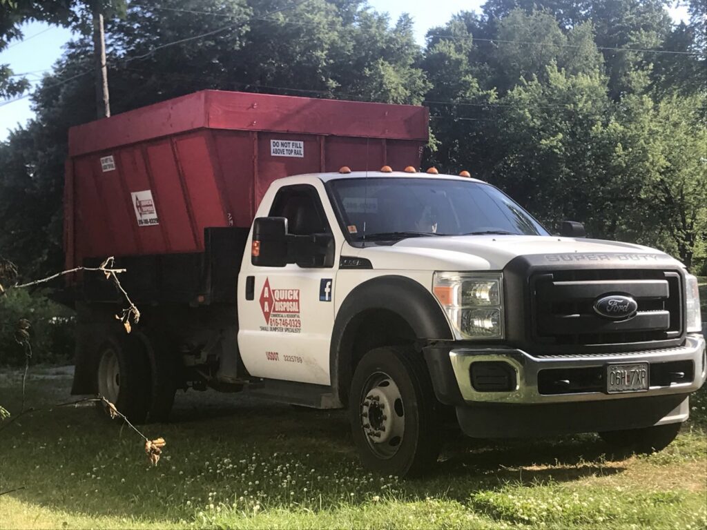 An AA Quick Disposal truck with a red dumpster on its bed, ready for junk removal in Kansas City, MO.