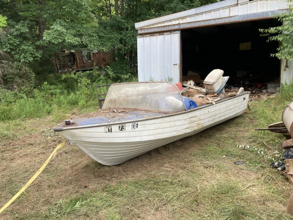 An old, abandoned boat sitting on land next to a shed, ready for junk removal by AAA Rousse Junk Removal Services Inc of Florida in Tampa, FL.