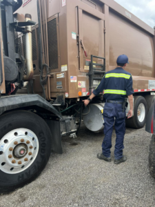 An AC Disposal LLC worker in uniform standing next to a large brown garbage truck in San Antonio, TX.