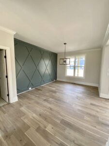 An empty room showcasing a dark green accent wall with a geometric pattern and newly installed hardwood flooring by Rapid Restoration and Construction in Mesa, AZ.