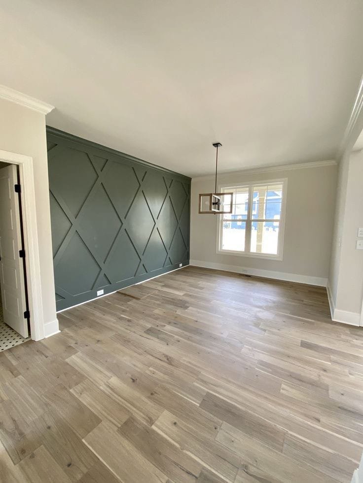 An empty room showcasing a dark green accent wall with a geometric pattern and newly installed hardwood flooring by Rapid Restoration and Construction in Mesa, AZ.