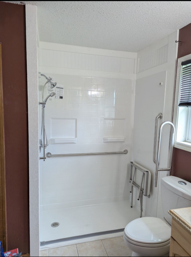An accessible shower with a folding seat and grab bars installed by Louisiana Special Needs Consultants, LLC in Opelousas, LA.