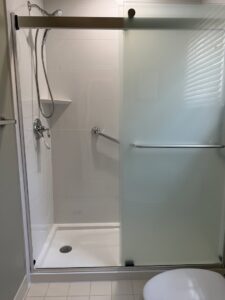 An accessible shower installation with white tiles, grab bars, and a frosted glass sliding door by Peninsula Bath & Tile in Salisbury, MD.