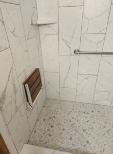 An accessible fold-down shower seat and grab bar installed in a tiled shower by Tim's handyman service in Cherry Hill, NJ.