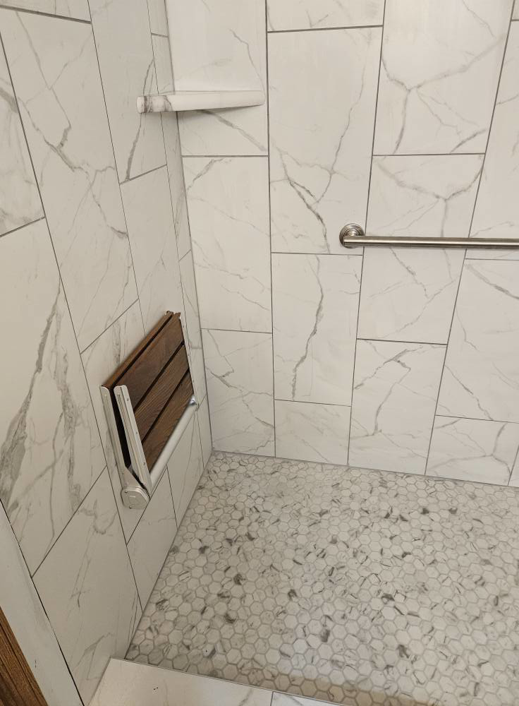 An accessible fold-down shower seat and grab bar installed in a tiled shower by Tim's handyman service in Cherry Hill, NJ.