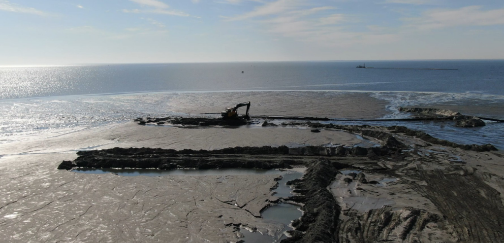 An aerial view of an excavator working on dredged material next to the water for Gator Dredging in Clearwater, FL.