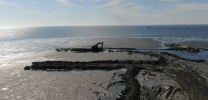 An aerial view of an excavator working on dredged material next to the water for Gator Dredging in Clearwater, FL.