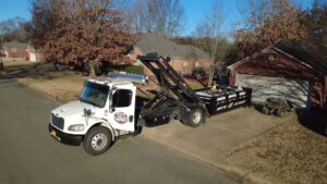 An aerial view of an American Dumpster Rentals truck deploying a black dumpster in a residential driveway in Morrilton, AR.