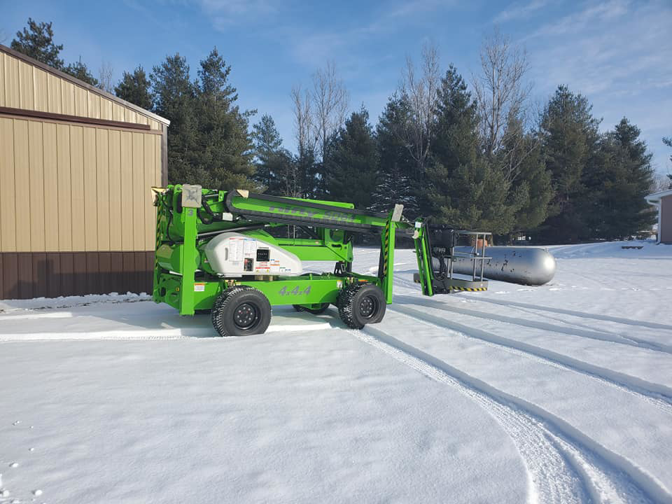 An aerial lift deployed at a tree removal site with cut branches on the snowy ground by Beaver Tree Service in Des Moines, IA