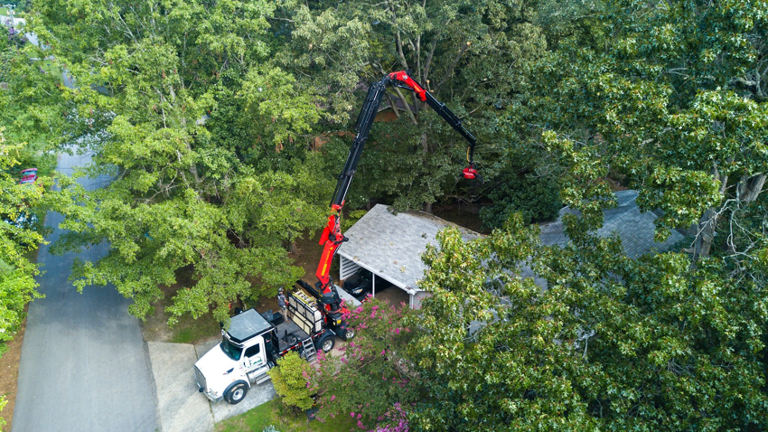 An aerial view of a crane truck performing tree removal services over a house by Explore Tree Service in Durham, NC.