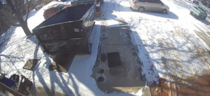 An aerial view of a Humpty Dump Roll-Offs & Dumpsters dumpster being placed or picked up in a snowy residential driveway in Commerce City, CO.