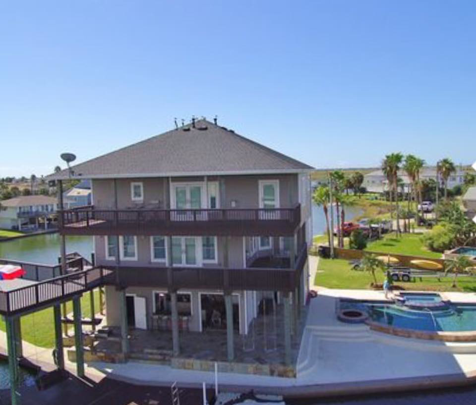 An aerial view of a grey waterfront custom home and pool area by Whitley Construction Services, a general contractor in Houston, TX.