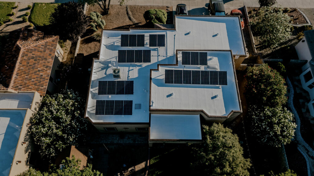 Aerial view of a residential house with a white flat roof and solar panels by Campos & Son Roofing and Construction in El Paso, TX