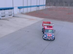An aerial view of a Waste Removal USA truck with a loaded red roll-off dumpster for general junk removal in Austin, TX