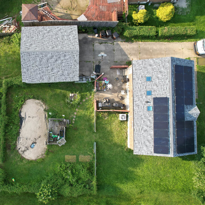 An aerial view of a house and garage with new gray shingle roofs and solar panels installed by GOAT Services, LLC in Louisville, KY.