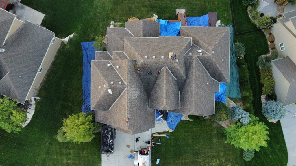 Aerial view of a residential roof repair with blue tarps and materials on the ground by Element Enterprises in Kansas City, MO.