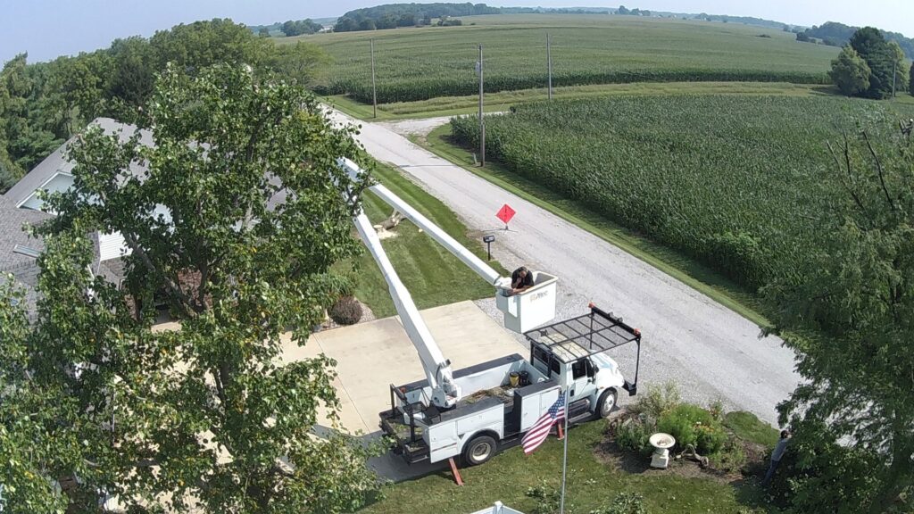 An aerial view of a worker in a bucket truck performing tree trimming near a residential home for Crockett's Tree Service in Lafayette, IN.