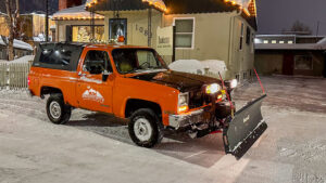 An AK Property Maintenance, Inc. snowplow truck with the company logo is parked in front of a building in Anchorage, AK.