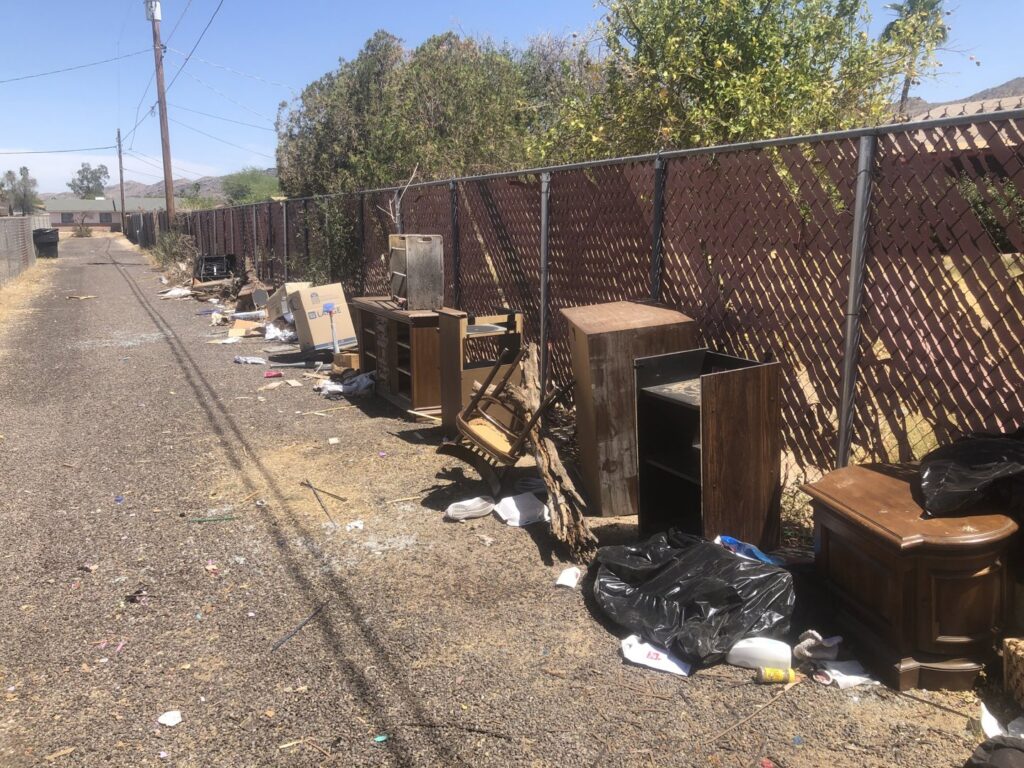 An alleyway cluttered with discarded furniture and trash bags, ready for Skunky's Junk Removal in Tempe, AZ.
