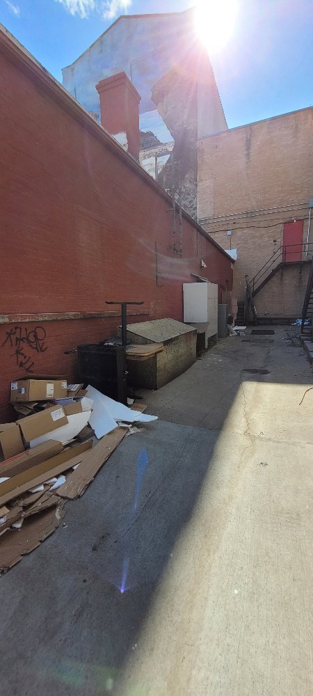 An alleyway filled with debris, cardboard, and old appliances, ready for removal by Clean Sweep Junk Removal in Augusta, ME.