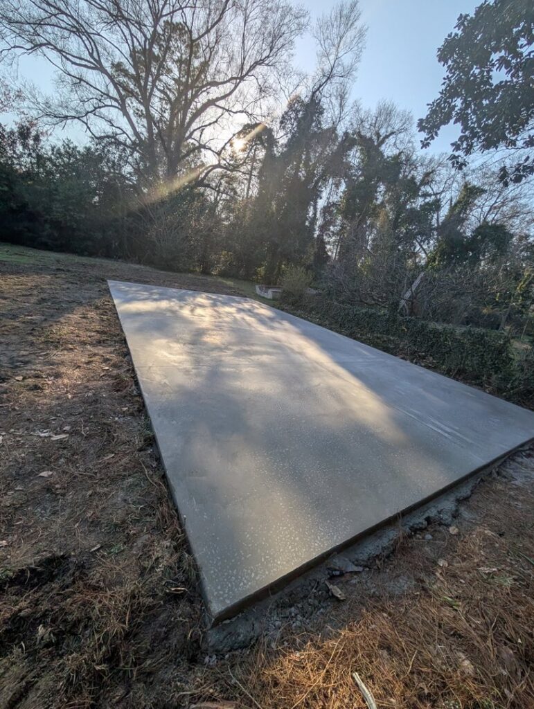 An angled view of a newly poured concrete pad in a backyard, installed by Allen's Concrete Finishing in Rock Hill, SC.