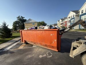 An orange dumpster filled with junk in a parking lot next to apartment buildings for removal by Lil Man W/A Can LLC in Columbus, OH.