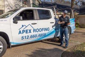 An APEX Roofing contractor standing next to a company truck, inspecting a site with a tablet, in Georgetown, TX.