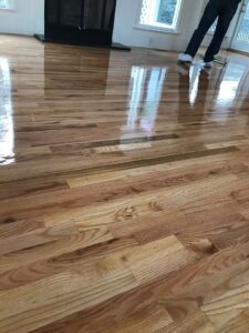 A shiny, newly finished hardwood floor, with a person in the background, indicating a completed job by Franco's Hardwood Flooring in Durham, NC.