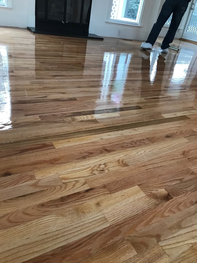 A shiny, newly finished hardwood floor, with a person in the background, indicating a completed job by Franco's Hardwood Flooring in Durham, NC.