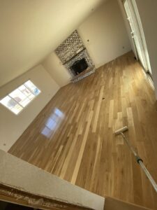 A large room with a newly finished hardwood floor, showing a roller used for applying finish by IHS flooring LLC in Brighton, CO.