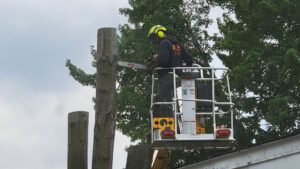 An arborist using a chainsaw from a bucket lift to remove a tree section for L. Moore Tree Service in Auburn, NY.