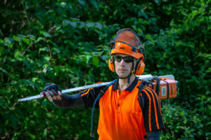 A professional arborist in safety gear holding a chainsaw, ready for tree work with Kansas Tree Care in Lawrence, KS.
