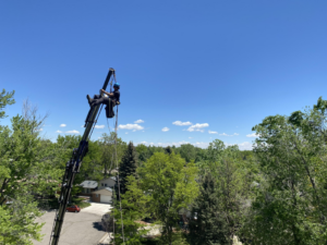 An arborist suspended from a crane arm performing tree removal services for Parkview Tree Service in Sheridan, WY.