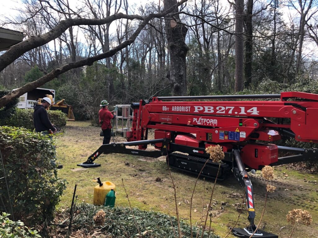 Tree service workers with a red tracked arborist platform preparing for tree work in a residential yard for State Tree Services, Inc in Sumter, SC.