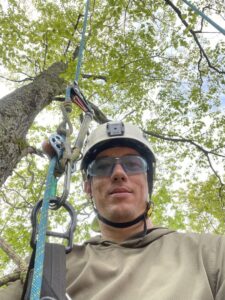A close-up selfie of an arborist wearing a helmet and safety glasses, ready for tree work with Lichen Trees in Brattleboro, VT.