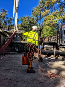 An arborist in full safety gear with ropes and a tree service truck, ready for work by Lone Star Arborists in Jackson, MS