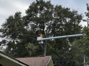 An arborist in a bucket lift performing tree trimming services over a residential roof for State Tree Services, Inc in Sumter, SC.