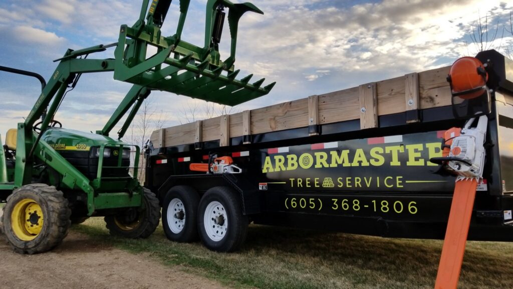ArborMaster Tree Service equipment, including a tractor with a grapple and a branded dump trailer, ready for tree work in Sioux Falls, SD.