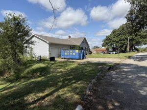 An ASAP Containers inc. truck with a hook lift system and blue dumpster at a commercial site for junk removal in Omaha, NE.