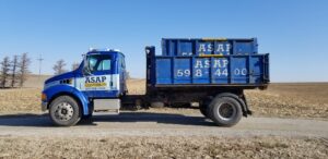 An ASAP Containers inc. truck with a blue dumpster on a dirt road, providing junk removal services in Omaha, NE.