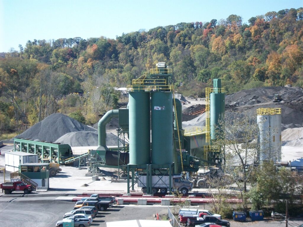 An asphalt production plant facility with large silos and aggregate piles, operated by Northeast-Paving in Bangor, ME