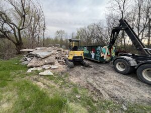An AT Disposal dumpster and excavator removing concrete debris from a site in Dewitt, IA.