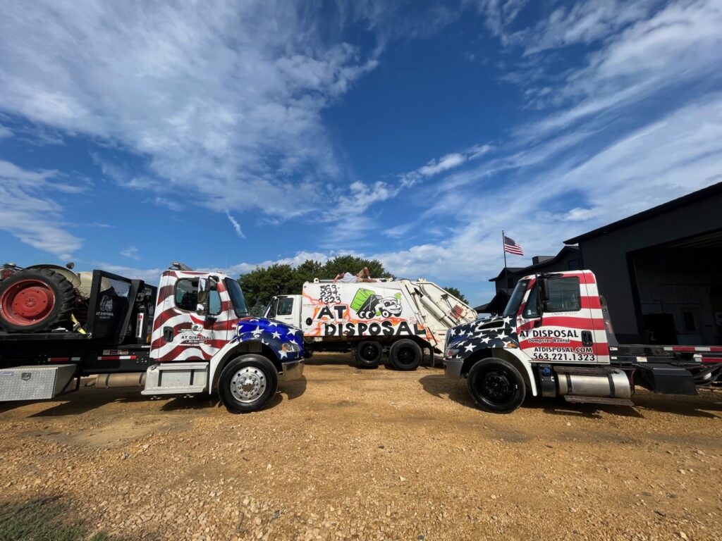 A fleet of AT Disposal junk removal and waste management trucks parked under a clear sky in Dewitt, IA.