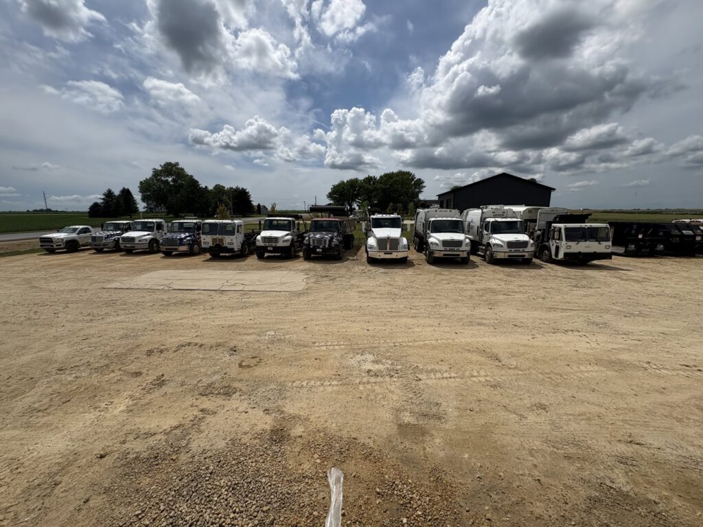 A large fleet of AT Disposal trucks, including garbage and roll-off trucks, parked in Dewitt, IA.