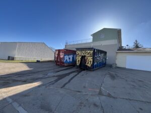 Two AT Disposal roll-off dumpsters parked at a commercial or industrial site in Dewitt, IA.