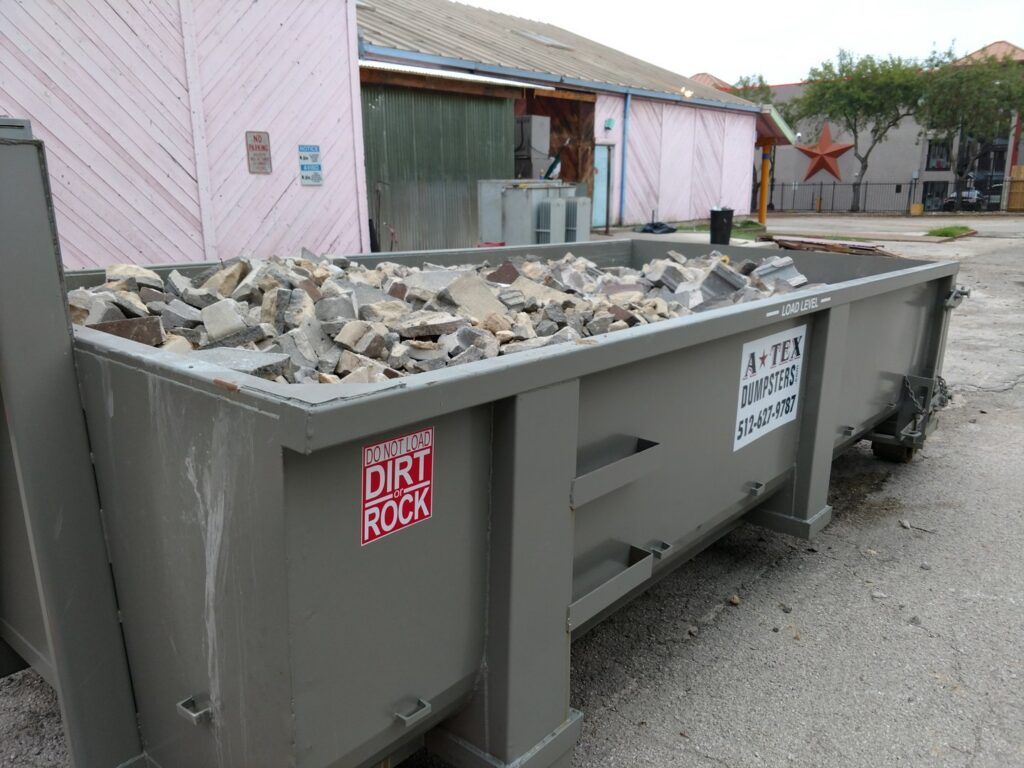 An ATEX Dumpsters Services roll-off dumpster filled with concrete and tile debris in Austin, TX.
