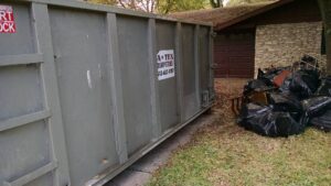 An ATEX Dumpsters Services roll-off dumpster placed next to a pile of trash bags for junk removal in Austin, TX.