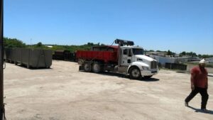 An ATEX Dumpsters Services truck with a red dump bed and a gray roll-off dumpster in Austin, TX.