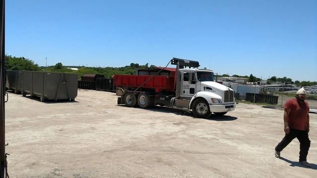 An ATEX Dumpsters Services truck with a red dump bed and a gray roll-off dumpster in Austin, TX.